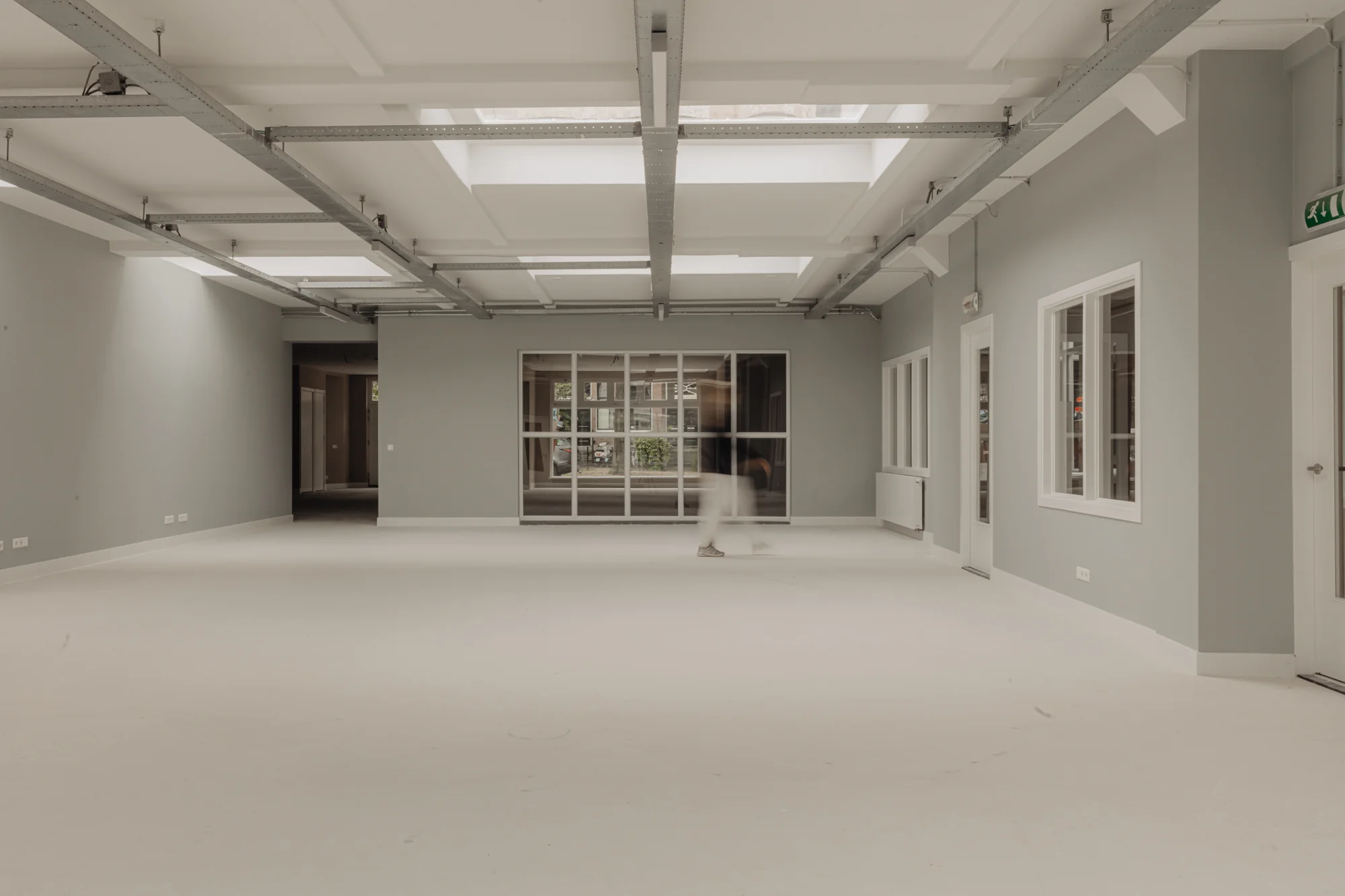 Licht en modern interieur van een leeg kantoorpand aan de Henri Polaklaan met grote ramen en zichtbare plafondconstructie.